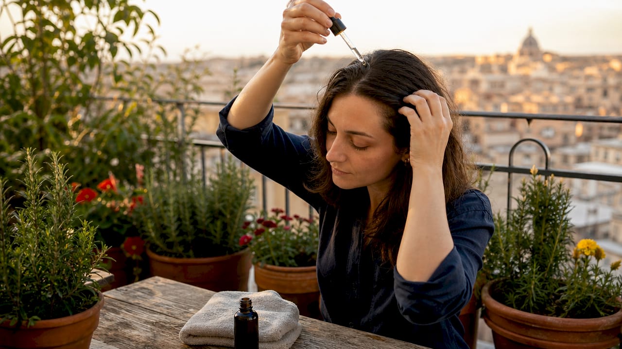 Woman applying rosemary oil to scalp at home