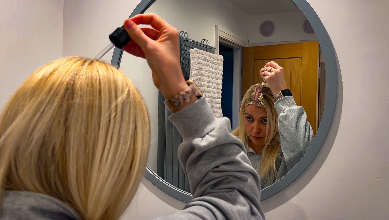 Woman applying hair growth serum to thinning hair while checking scalp in mirror
