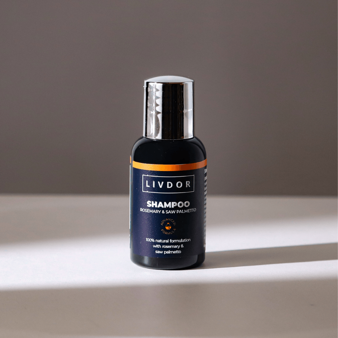 A travel size bottle of LIVDOR Rosemary & Saw Palmetto Shampoo, featuring a dark navy blue label with a metallic silver cap, set against a neutral gray background with a soft shadow.